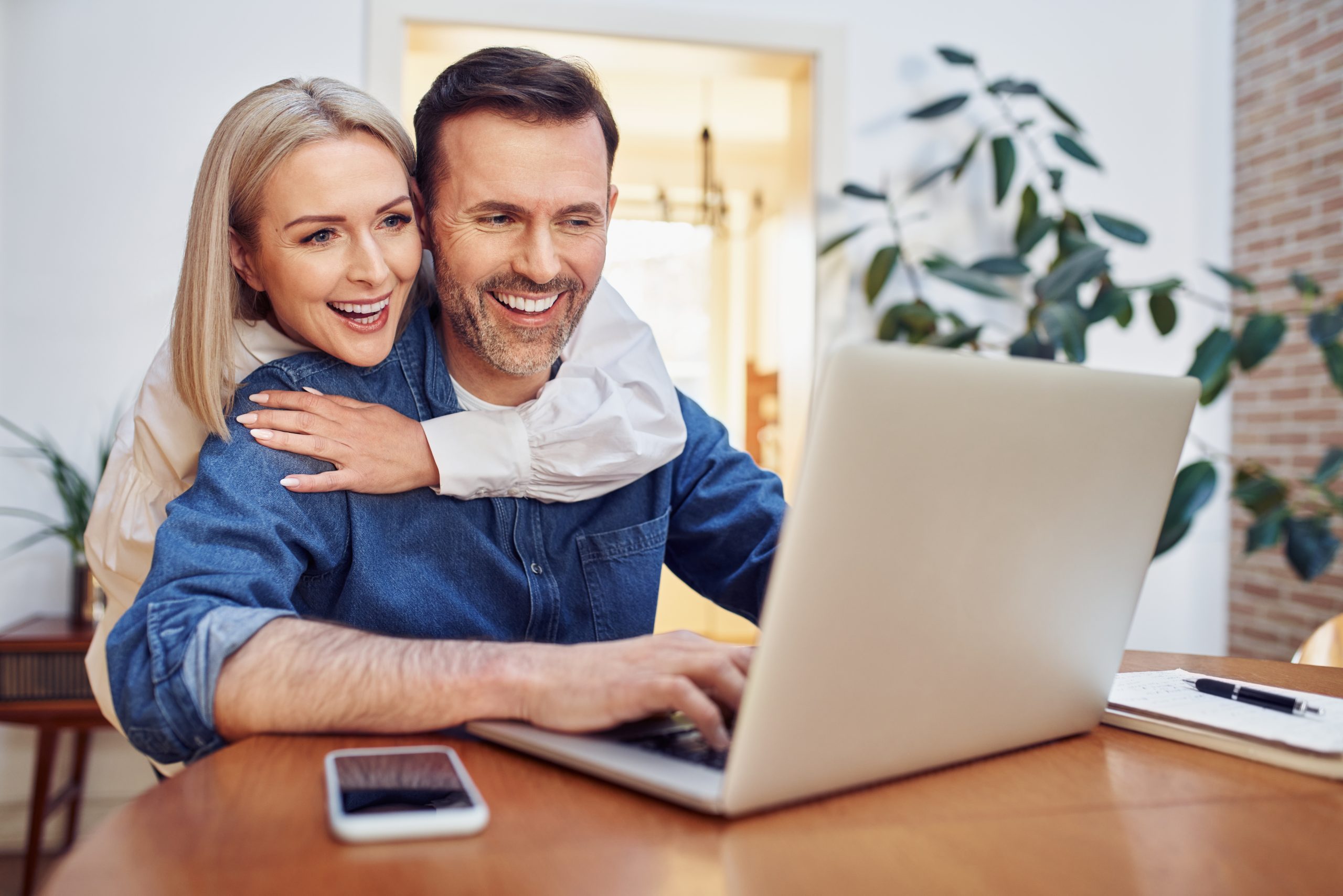 Happy mid adult couple at home using laptop surfing the net